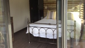 A bedroom with a metal bed frame, a wooden slatted ceiling, and a glass door leading to an outdoor area.