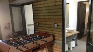 A room with a wooden wall, a foosball table, a sink, and a small stool.
