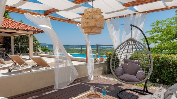 Une terrasse en bois avec un fauteuil suspendu, des chaises longues et une table sur laquelle se trouvent une boisson et un menu.