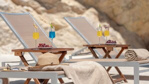 Deux chaises de plage, avec des serviettes et des boissons posées sur une table, le tout sur fond de paysage rocheux.