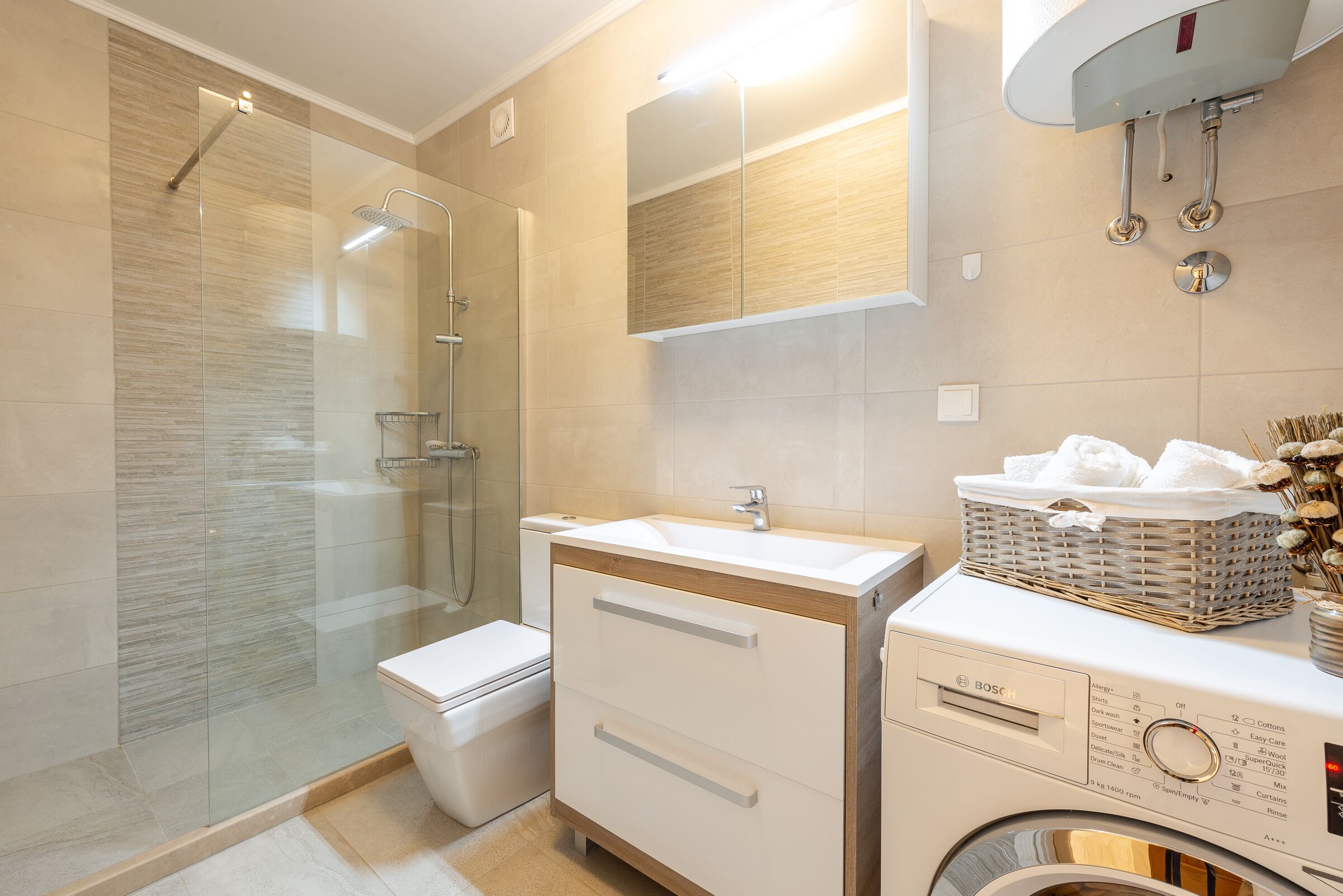Ein modernes Badezimmer mit Duschkabine aus Glas, Toilette, Waschbecken mit Spiegel und einer Waschmaschine.