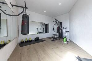 Een sportschool met een bokszak, kettlebells, een spiegel en trainingsapparatuur.