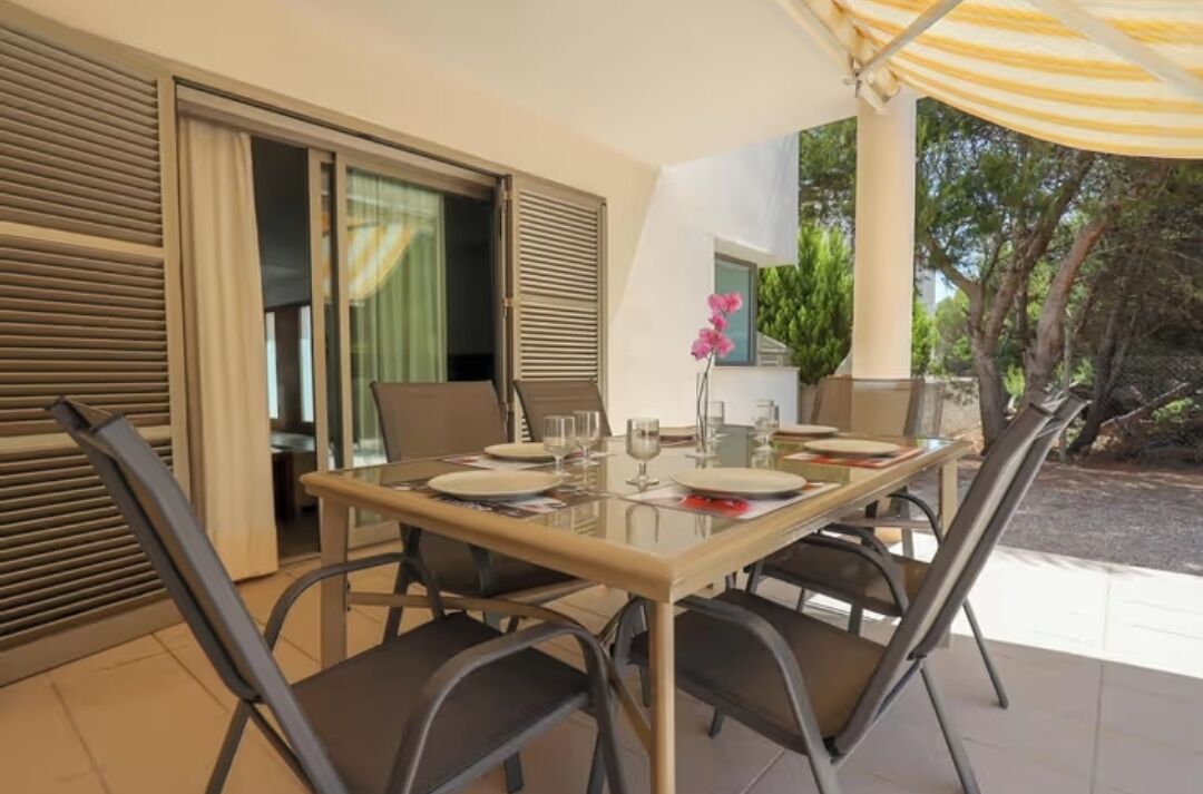 Un coin repas avec une table en verre, des chaises et un parasol jaune.