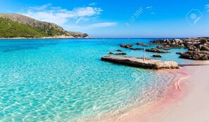 Ein klares, türkisblaues Meer mit felsiger Küste und einem Sandstrand.