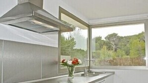 A modern kitchen with a stainless steel range hood, a window with a view of greenery, and a vase with flowers on the counter. - Large aloe house (Son Serra de Marina)