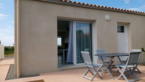 Eine Terrass mit Tisch, Stühlen, einer Schiebetür aus Glas und einem kleinen Fenster.