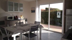 Eine moderne Küche mit Essbereich, einer Mikrowelle, einer Kaffeemaschine und Blick auf einen Garten durch eine Glastür.