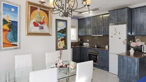 Une cuisine moderne avec des meubles de couleur sombre, une table à manger en verre et un lustre.