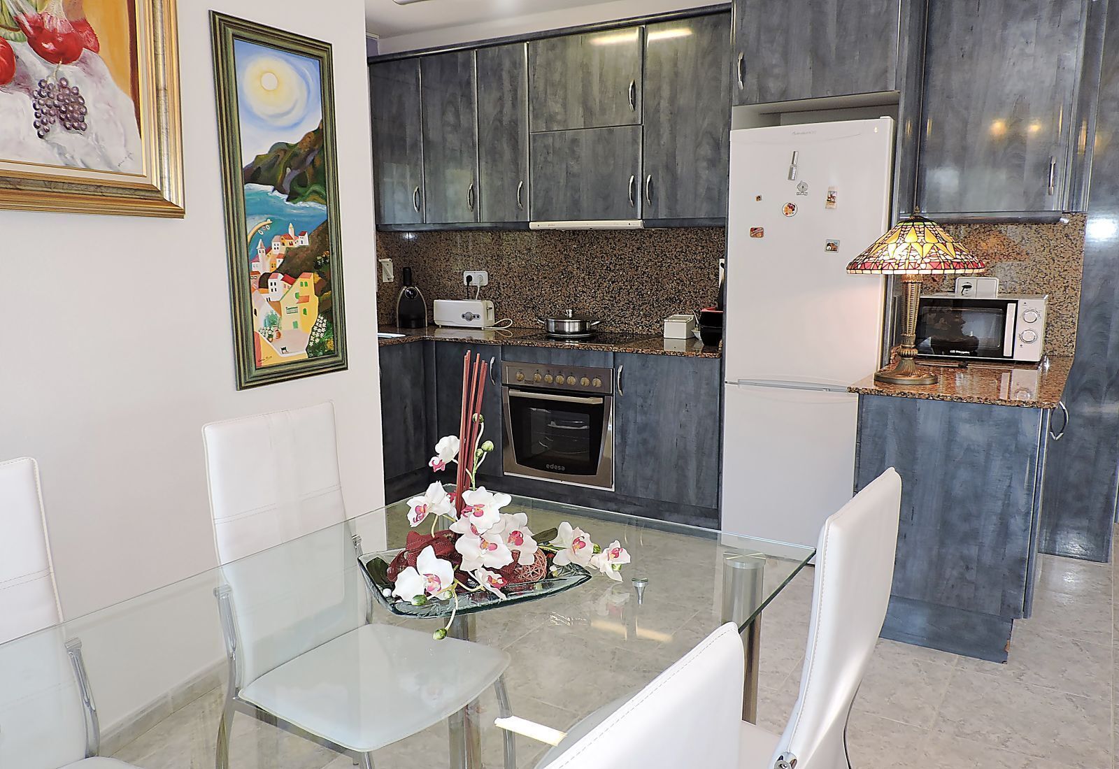 A modern kitchen with dark cabinets, a microwave, an oven, and a glass dining table with chairs.