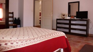 Een slaapkamer met een bed, een dressoir, een televisie en een deur naar een andere kamer.
