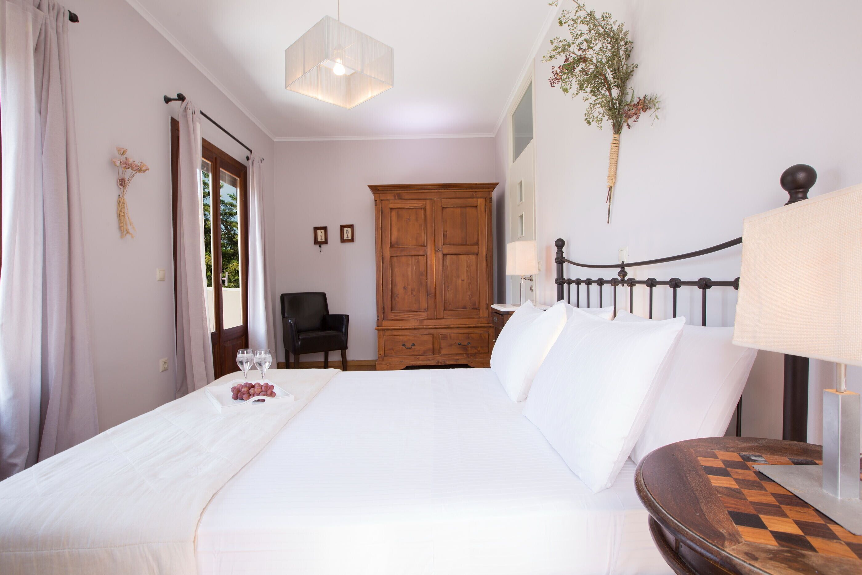 Un dormitorio ordenado con una cama grande, un armario de madera, una silla y una mesita de noche con una lámpara.