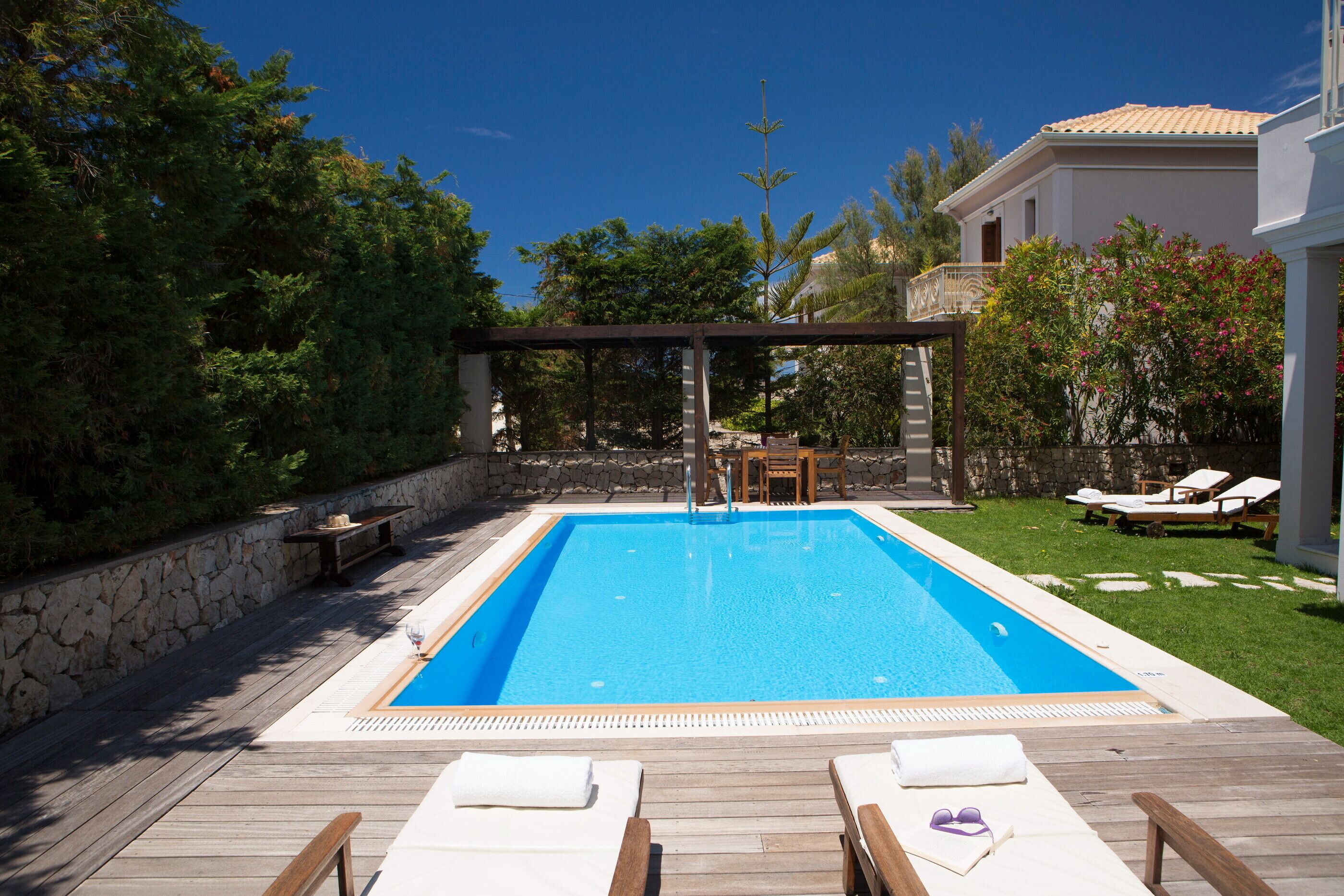 A rectangular swimming pool with a wooden deck and lounge chairs.