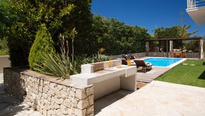 Zona de piscina amb mur de pedra, terrassa de fusta i seients amb taula i cadires.