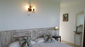 Ein Schlafzimmer mit einem Holzkopfteil, zwei Kissen mit tropischen Mustern, einer Nachttischlampe und einem kleinen Tisch mit einer Lampe.