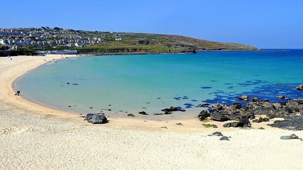 A coastal beach with clear turquoise waters, a sandy shore, and rocky outcrops.