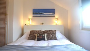 A neatly made bed with a striped bedspread, a headboard with a painting of a beach scene, and two wall-mounted lamps.