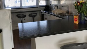 A modern kitchen with white cabinets, a black countertop, and a window with blinds.
