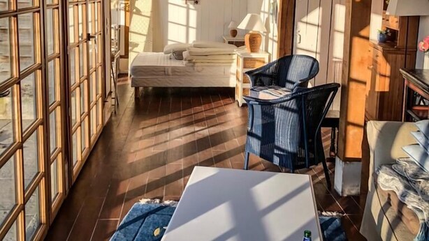 Une pièce chaleureuse avec un plafond en bois, un lit, une table avec une bouteille et une chaise.