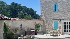 Un bâtiment en pierre avec un toit en tuiles, une terrasse avec des meubles d’extérieur et un jardin agrémenté de fleurs.