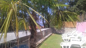 Un espacio al aire libre cercado con piscina, un muro de piedra y sillas de plástico blanco.
