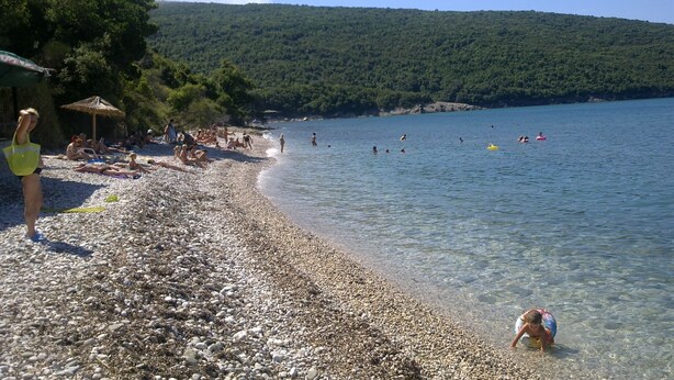 Una playa de guijarros con gente tomando el sol y nadando.