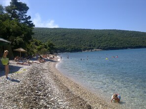 Une plage de galets où des gens se prélassent au soleil et se baignent.