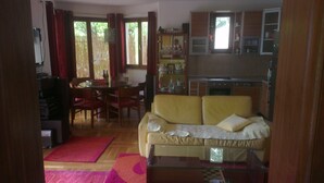 Una sala de estar con un sofá amarillo, una mesa de comedor con sillas y una zona de cocina con armarios y un ventanal.