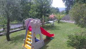Un parque infantil con tobogán y estructura de escalada, rodeado de árboles y una valla.