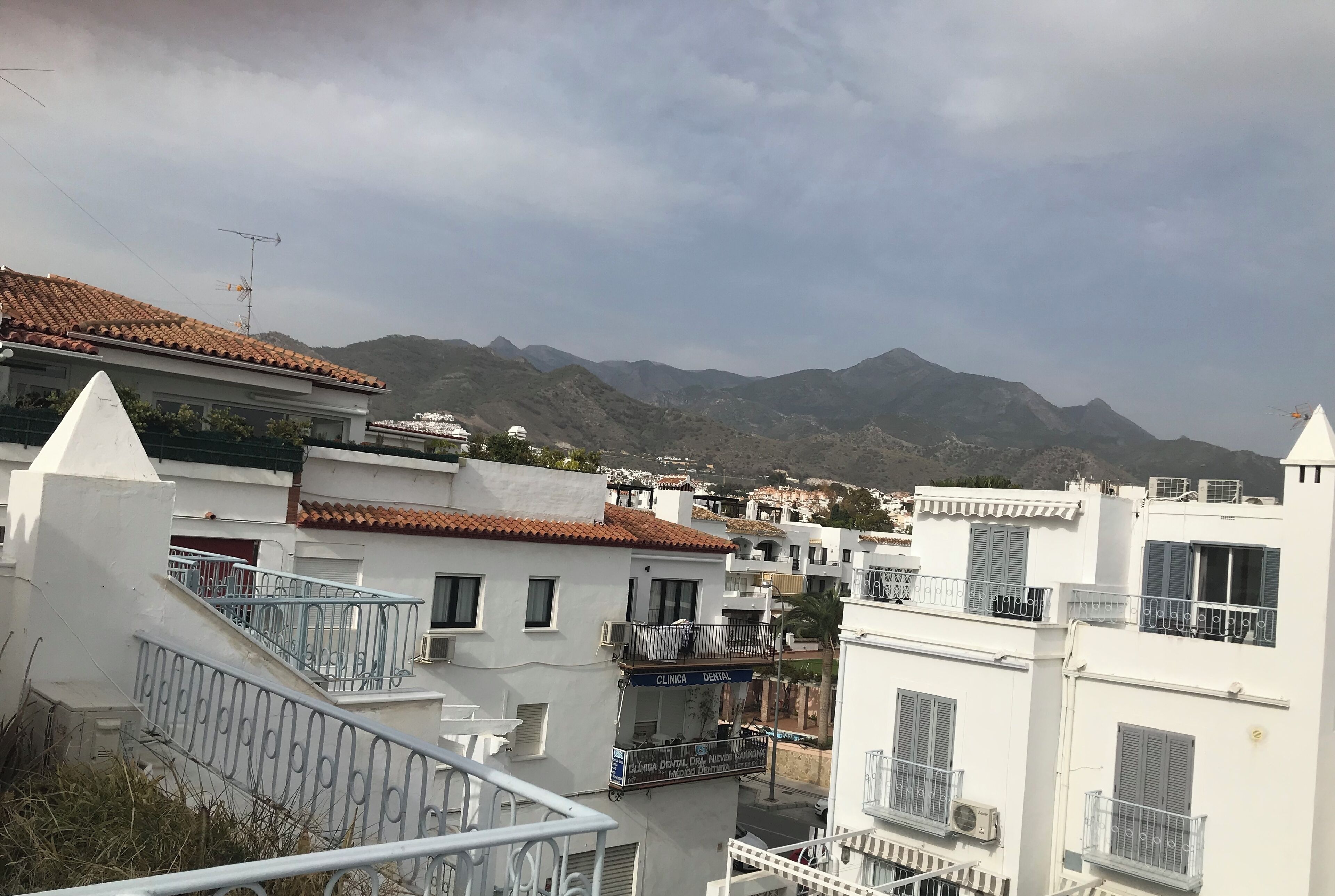 Un quartier résidentiel caractérisé par des bâtiments blancs, des balcons et un paysage montagneux en arrière-plan.