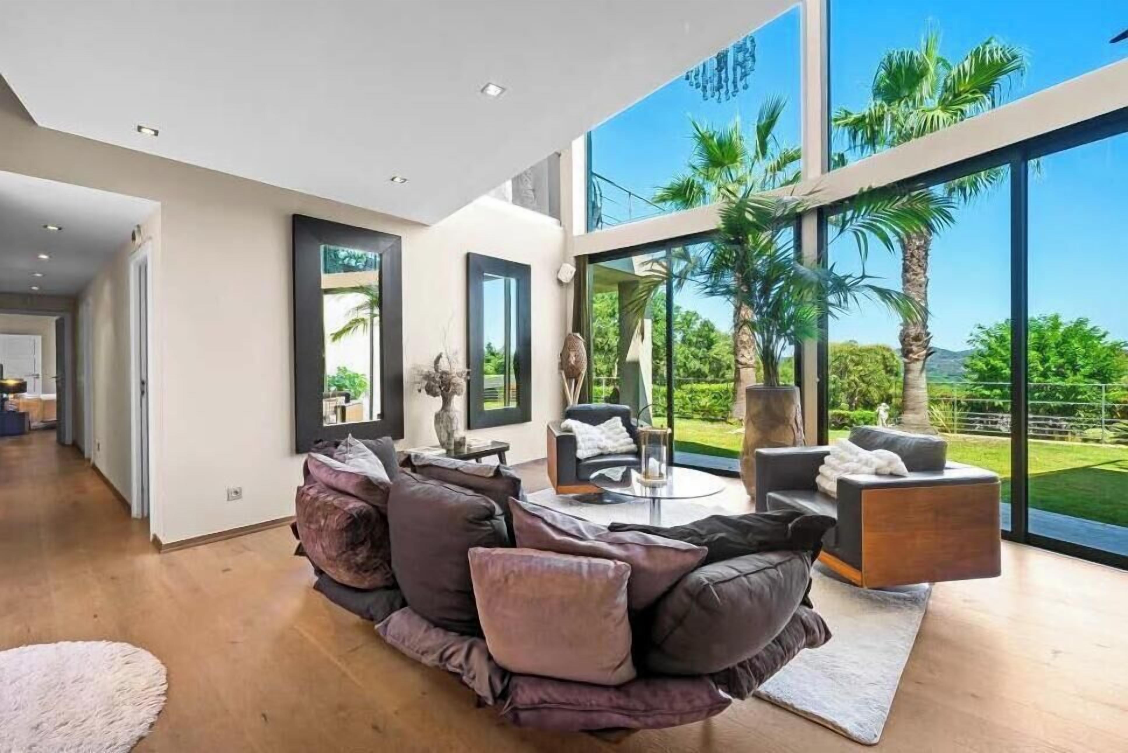 A modern living room with a sectional sofa, a coffee table, and a view of palm trees through large windows.