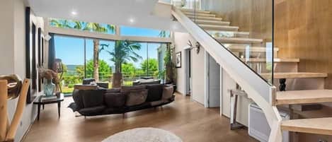 Amplia sala de estar con una escalera moderna, ventanas grandes y vistas a zonas verdes.