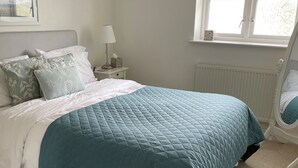 Et soveværelse med seng, natbord, lampe og et vindue med udsigt til træer.