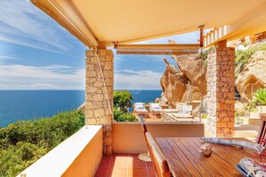 A terrace with stone pillars, a wooden table, and lounge chairs overlooking the sea. - Villa Josephine with pool in Costa Paradiso (Costa Paradiso)
