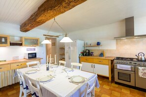 A kitchen with wooden beams, white cabinets, a dining table set for four, and a stove.