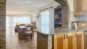 A kitchen with a stone archway, wooden cabinets, and a dining area with chairs and a table.