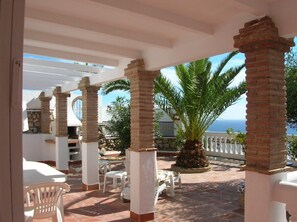 A covered outdoor area with white chairs and a palm tree, overlooking a body of water. - Beautiful villa, panoramic views of sea and mountains, close to town (almunecar,)
