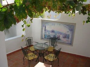 A patio with a round glass table and four chairs, surrounded by a white wall and a large landscape painting. - Beautiful villa, panoramic views of sea and mountains, close to town (almunecar,)