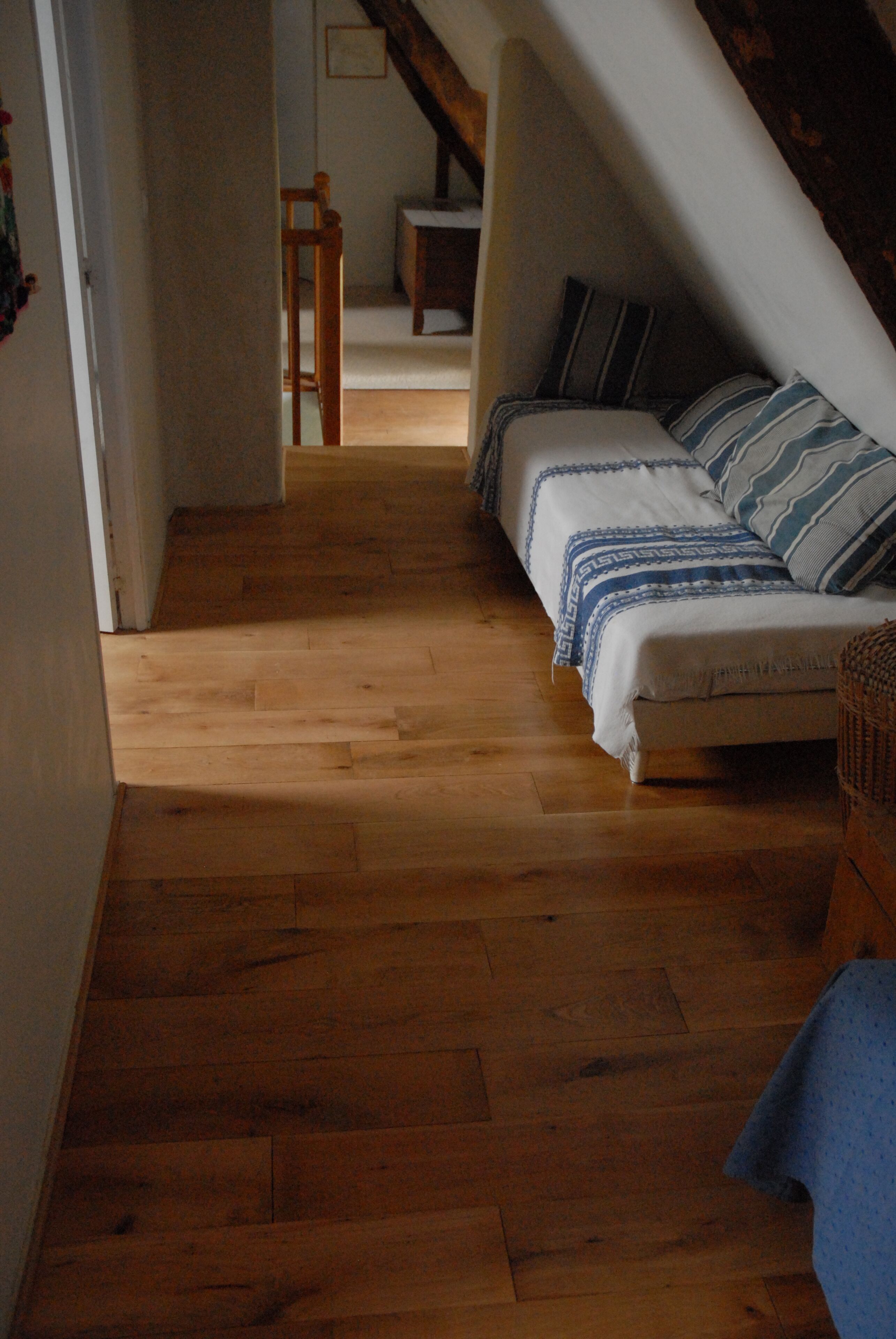 Ein schmaler Korridor mit Holzboden, der zu einem Schlafzimmer mit Bett und Stuhl führt.