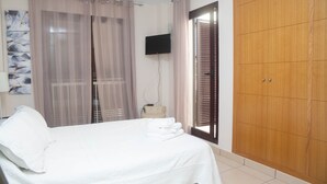 Quarto com cama, televisão fixada na parede, guarda-roupa e janela com cortinas.