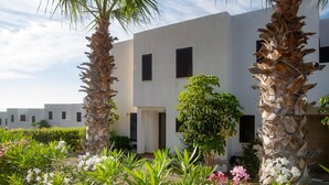 Um edifício moderno com paredes brancas e persianas pretas, rodeado por vegetação exuberante e plantas floridas.