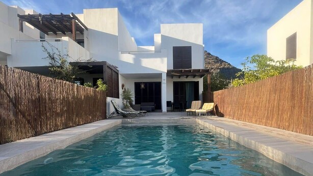 Uma casa moderna com piscina, cerca de madeira e montanhas ao fundo.