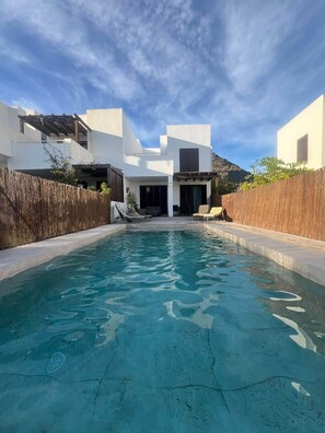 Une maison moderne avec une piscine, une clôture en bois et une montagne en arrière-plan.
