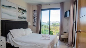 Quarto com cama grande, mesa de cabeceira, cadeira, televisão e vista da cidade.