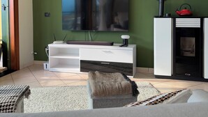 Ein modernes Wohnzimmer mit einem an einer grünen Wand befestigten Flachbildfernseher, einer weißen Unterhaltungseinheit mit einem roten Wasserkocher und einem Kamin.