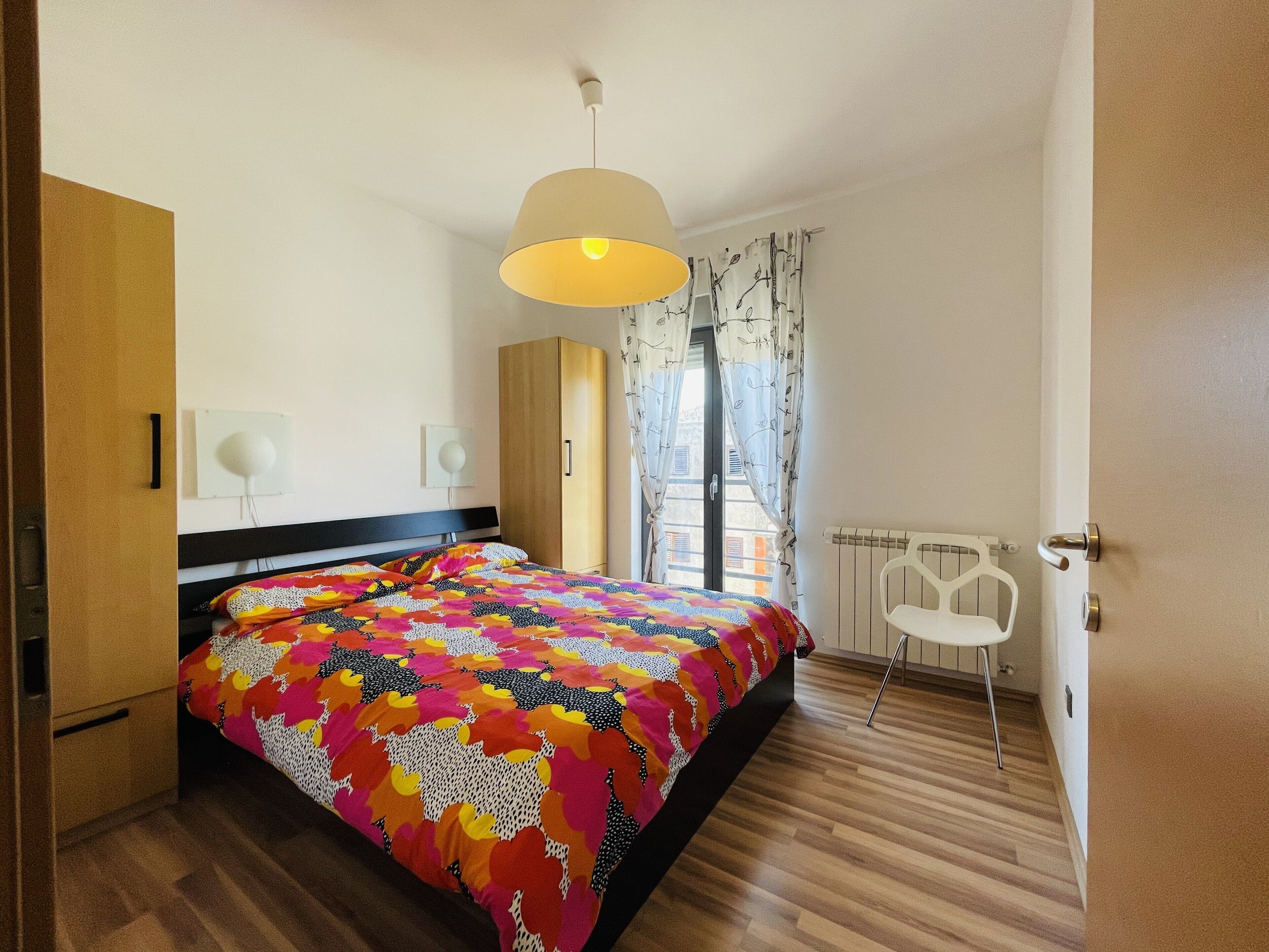 A bedroom with a bed, a wardrobe, a radiator, and a chair.