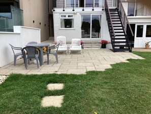 Uma área de pátio com mesa e cadeiras, uma escadaria e um prédio com varanda.