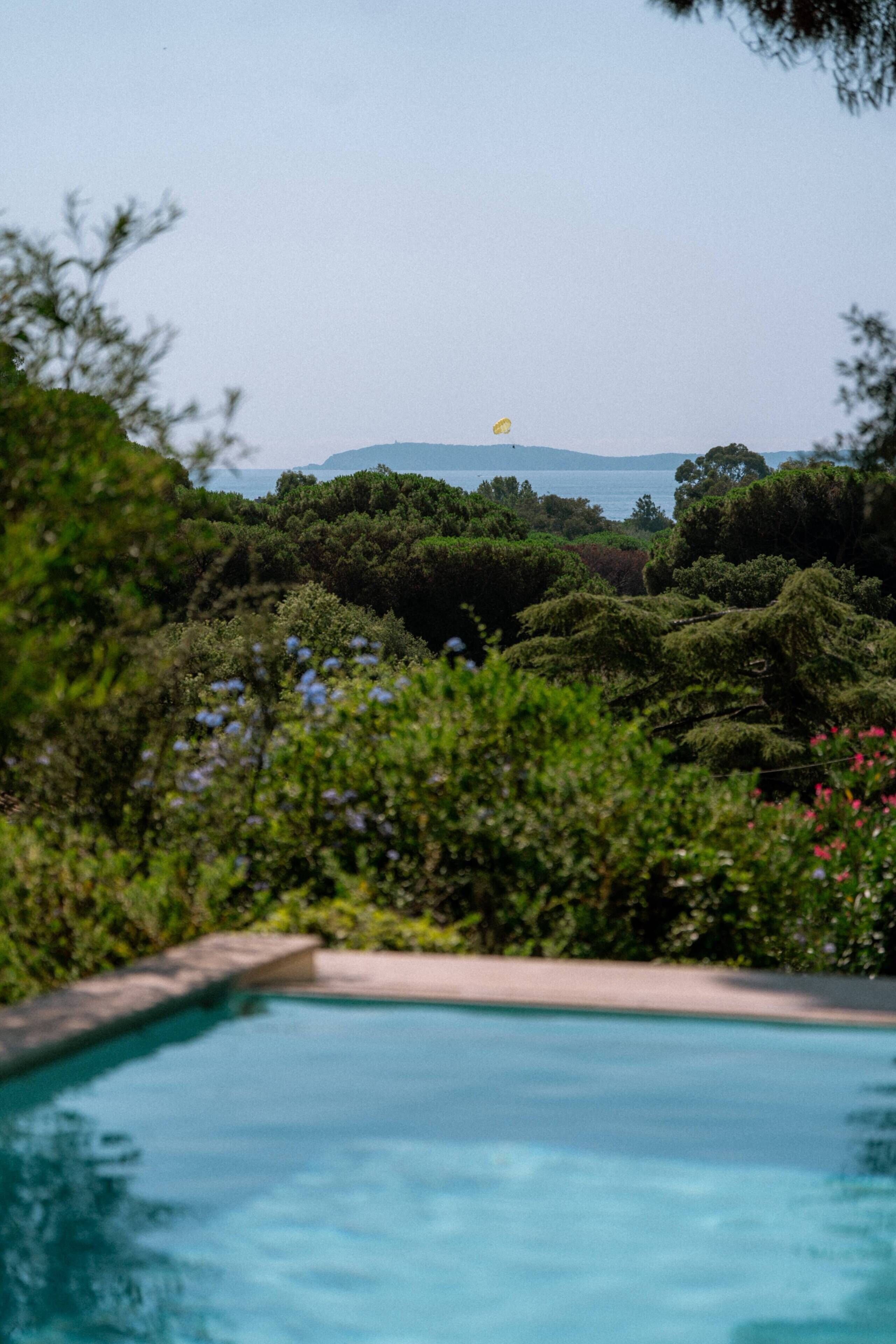 A swimming pool surrounded by lush greenery and a view of the sea.
