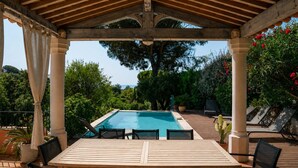 Een buitenzwembad met een houten pergola, zitplaatsen en weelderige begroeiing.