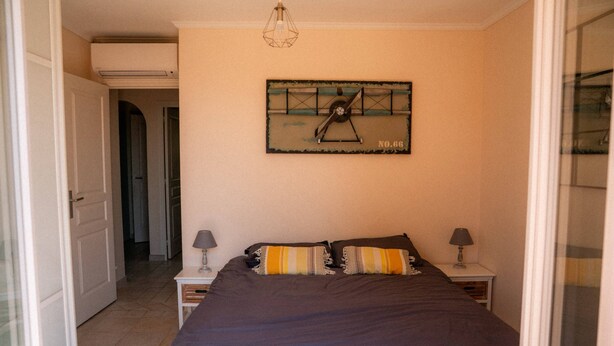 Een slaapkamer met een bed, twee nachtkastjes, een wandklok en een deur naar een andere kamer.