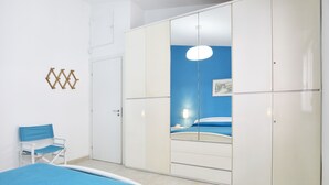 Un dormitorio con cama, una silla, armario y espejo.